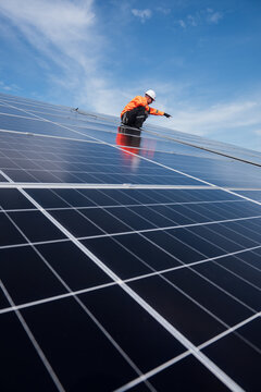 Technician installing solar panels on factory roof for green energy. A skilled technician in safety gear is working on a solar panel installation on rooftop.