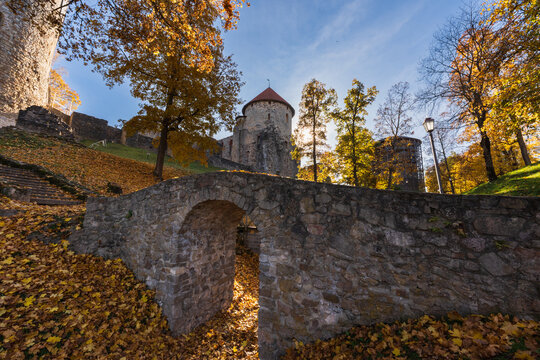 CESIS, LATVIA - OCTOBER 27, 2024: Ancient stone bridge and medieval castle fortifications surrounded by colorful autumn trees in Cesis.