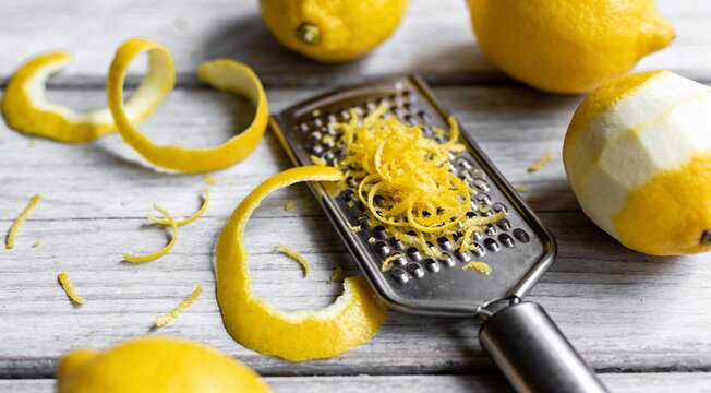 Fresh lemons with zest and zester tool on grey table, flat lay