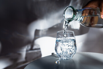 Pouring drinking water into glass on white table in morning sunlight.