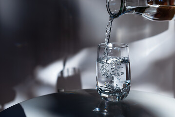 Pouring drinking water into glass on white table in morning sunlight.