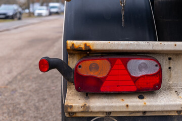 Rear view of a trailer with a rusty taillight on a quiet street during a cloudy day