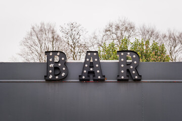 Illuminated bar sign shines against a cloudy sky with trees in the background at a cozy outdoor venue