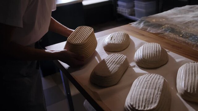 A baker inverts proofing baskets and places the formed dough on the counter before baking tartines. Manual fermentation, a professional process, the texture of raw dough, traditional baking.