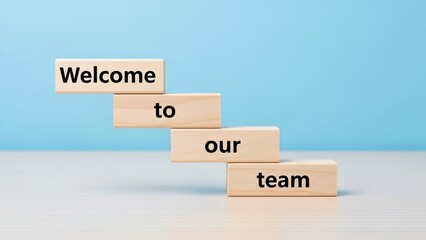 Wooden blocks spelling 'Welcome to our team' arranged like stairs on a white surface with a blue background, symbolizing new beginnings and teamwork.
