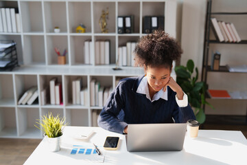 Young black woman seriously working on her laptop at an office desk, showcasing focus, education,...