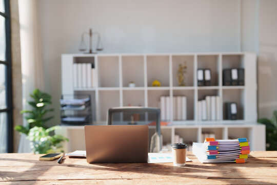 Law office desk featuring a laptop, stack of documents with colorful clips, coffee cup, and smartphone, emphasizing legal work and professional administration in a bright setting