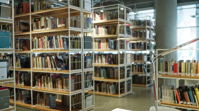 Library shelves with rows of books, metal racks and a desk lamp seen in soft bokeh, defocused shallow focus interior; background copyspace template calm.