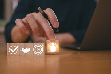 Businessman hand picks up wooden block showing the group of people icon in teamwork concept and block shows business goal, strategy, target, mission