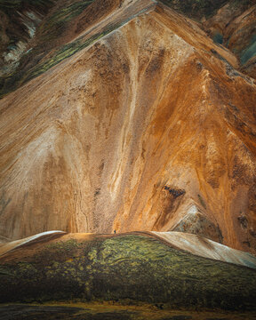 View of rugged, ochre-colored mountains, carved by time and weather, rise dramatically above the green and brown mossy landscape, Landmannalaugar,  Highlands, Iceland.