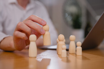 Choosing the Right Candidate Employee Selection Process. Businessman leader holding and choosing wooden people from a group of employees while working on laptop computer in office