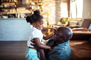 Senior grandfather lifting smiling child granddaughter in cozy living room