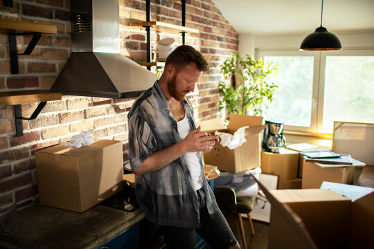 Adult man focused on phone while unpacking boxes in home kitchen
