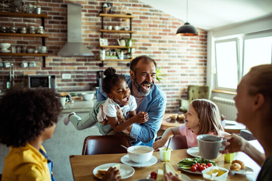 Adult father playing with happy children at breakfast in home kitchen