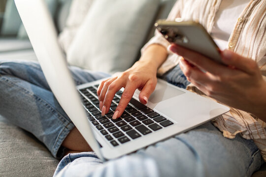 Adult woman focused typing on laptop and phone at home