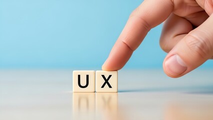 A human finger pointing at two small letter tiles spelling "UX" on a wooden surface with a blue background.