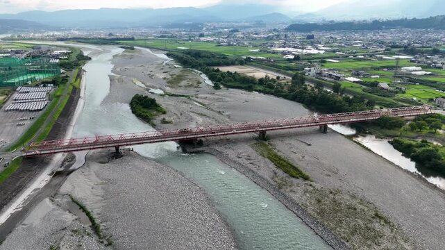A bridge spans a river with a city in the background. The bridge is red and spans the entire width of the river