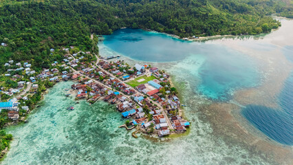 Drone view of tropical coastal village with turquoise lagoon, coral reefs and lush green hills