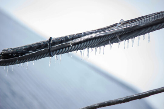 Icy icicles on electric wires against blue sky, freezing rain consequences.
