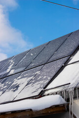Solar panels covered with snow and ice in winter, renewable energy in frost.