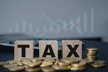 Taxation financial year preparation, wood blocks with word TAX and gold coins with blurred arrow up and down background