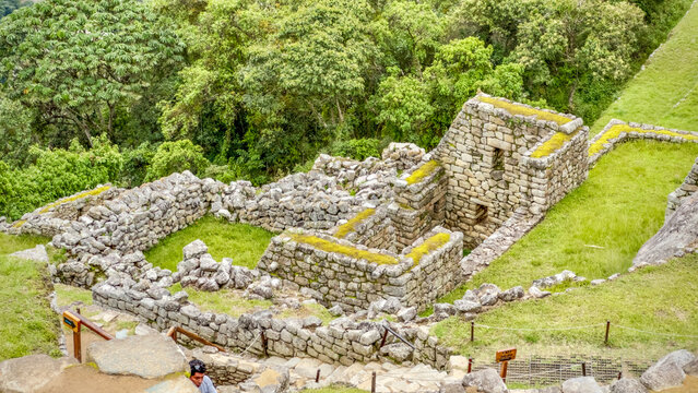 View of ancient stone structures, with moss-covered walls and steep terraces blending into the lush green mountainside, evoking the mystery of a lost civilization, Machu Picchu, Peru.