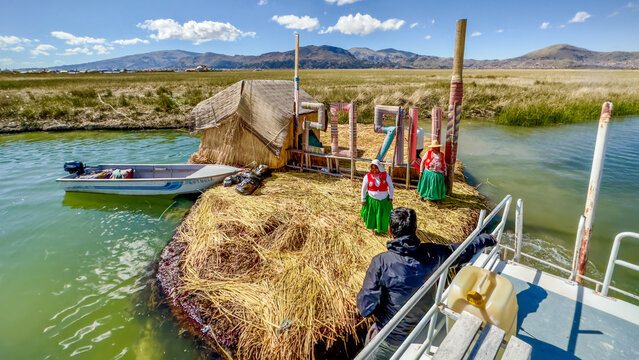 Lake Titicaca, Peru - 25 December 2024: View of a floating Uros island, its golden reeds contrasting with the turquoise waters, women in bright traditional dress, and distant Andean peaks.