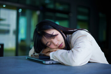 Young asian tired business woman wearing white stylish shirt taking a break and sleeping on laptop
