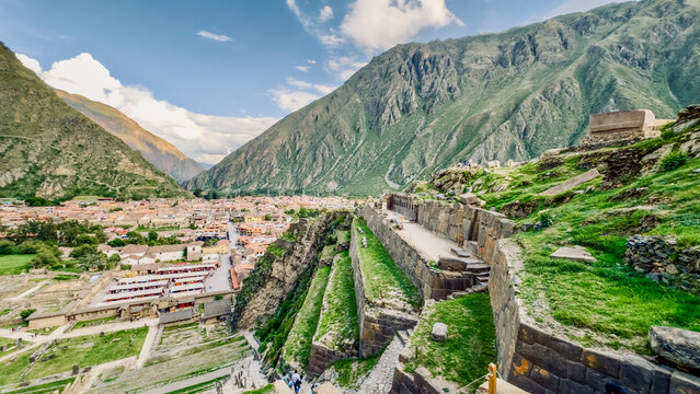 View of ancient stone terraces cascade down the mountainside, overlooking the quaint village nestled amidst the towering peaks, Ollantaytambo, Peru.