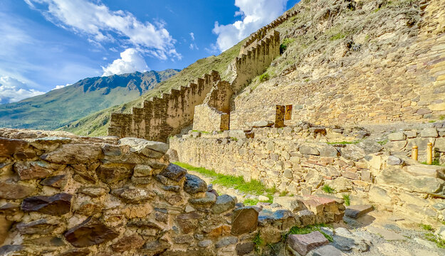 View of ancient stone walls climb the steep mountain face under a bright sky, a testament to history and human endeavor, Ollantaytambo, Peru.