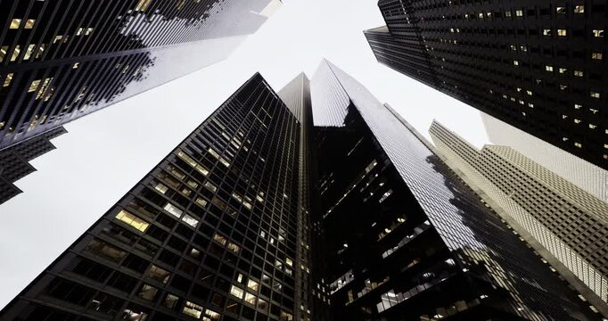 Modern buildings rise dramatically into the cloudy sky, showcasing glass facades and architectural design in a vibrant city during the late afternoon.