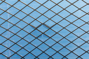 Modern glass roof construction with a geometric diamond pattern. Blue sky visible through a transparent architectural ceiling featuring a sleek steel frame and contemporary design