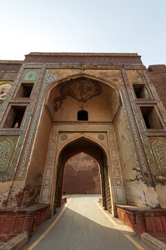 View of an ancient arched gateway adorned with intricate tile work stands proudly against a clear sky, inviting exploration in Lahore Fort, Punjab, Pakistan.
