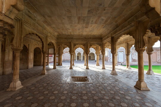 View of an ornately decorated courtyard featuring stone pillars and arched walkways, bathed in light and shadow, Lahore Fort, Punjab, Pakistan.