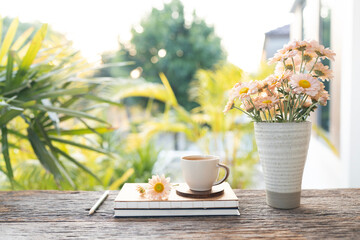 coffee cup and Chrysanthemum flowers in a vase and notebook on wooed table with garden view