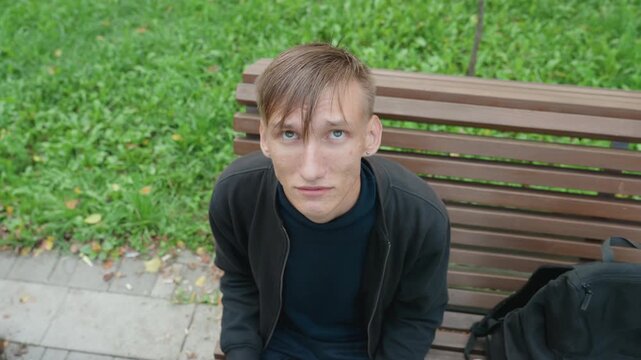 white man looking directly at camera, wet hair plastered, intense stare shifting to downward glance, hands on backpack while rehearsing monologue like actor, pausing like street performer, breath
