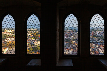 From a dark, historic interior, four arched, leaded windows frame a panoramic view