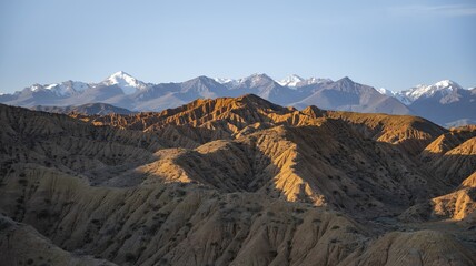 Landscape of eroded hills at sunrise, badlands, white mountain peaks of the Tian Shan Mountains in the background, Canyon of the Forgotten Rivers, Issyk Kul, Kyrgyzstan