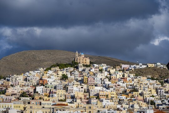 View of the town of Ermoupoli with pastel-coloured houses, on the hill Anastasi Church or Church of the Resurrection, dramatic cloudy sky, Ermoupoli, Syros, Cyclades, Greece