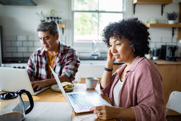 Mature couple focused on remote work in home kitchen