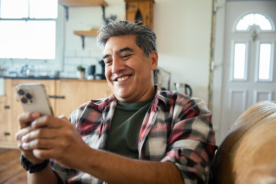 Mature man smiling at smartphone on sofa at home