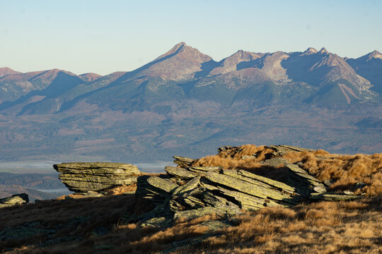 View of jagged rocks and golden grasses meet the distant, hazy mountain range under a clear sky, Stredna hola, Banskobystricky kraj, Slovakia.