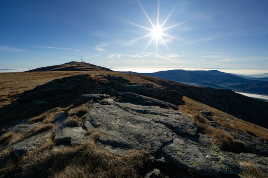 View of golden grasses clinging to rocky terrain under a bright sun, with distant mountains fading into the horizon, Stredna hola, Banskobystricky kraj, Slovakia.