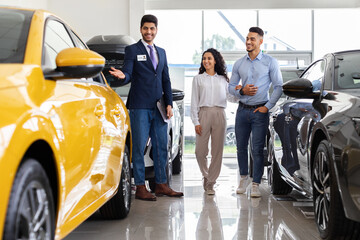 Wealthy middle-eastern young couple having conversation with good-looking sales assistant at auto...