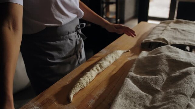 A baker rolls out dough by hand, shaping it into a baguette before baking. Baking classic French baguettes in an artisan bakery. Hand-crafting dough in a bakery. 