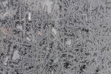 Frost patterns cover a window on a cold winter morning in a city, creating intricate designs and shapes from frozen moisture