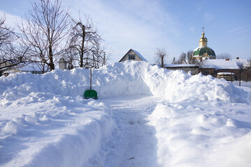 Winter scene in snowy landscape with a pathway cleared through large snowdrifts in a rural area during bright daylight