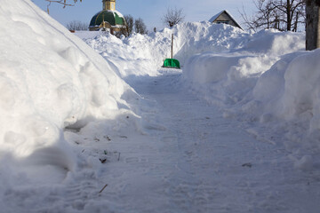 Snow-covered pathway leads to a building in winter time with piles of snow on both sides