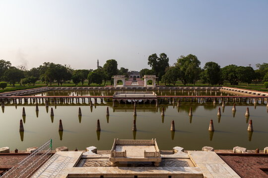 View of a serene reflection pool with symmetrical rows of pillars mirroring the sky amidst lush greenery, creating a tranquil scene, Lahore, Punjab, Pakistan.