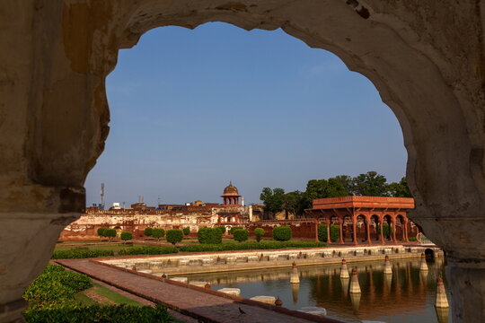 View of a tranquil pond reflecting a historic structure with red and white walls, framed by an ornate archway, GT Road, Lahore, Punjab, Pakistan.